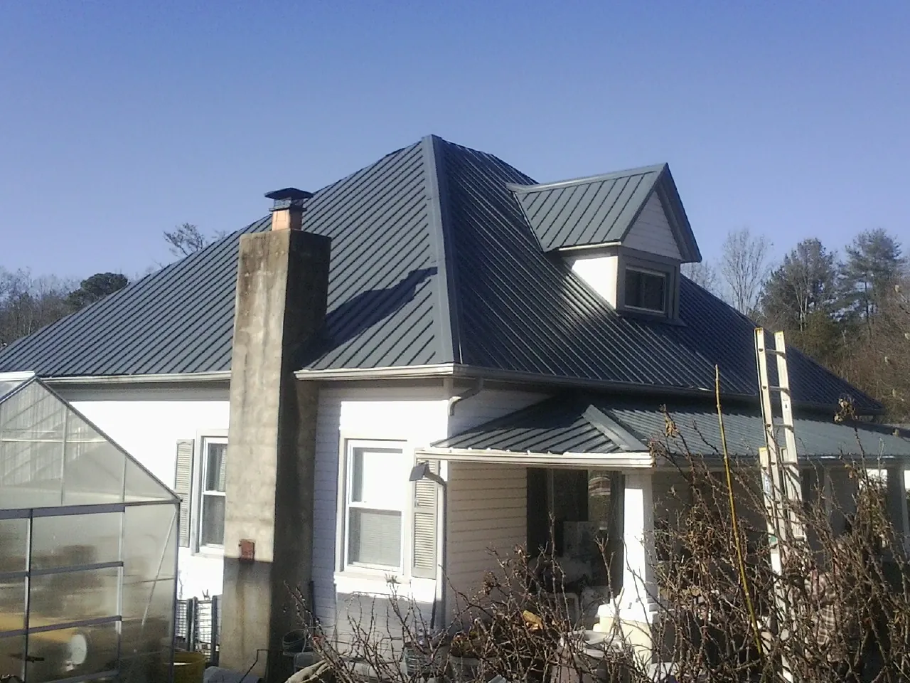 Dark blue standing seam metal roof on a white farmhouse with dormer — Slate & Tile Roof Repair by Roofing Brothers in Cincinnatus