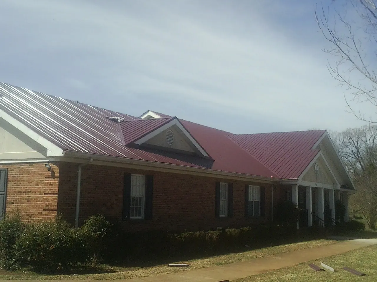 Red metal roof with gabled entries on a long brick building, from a Hail Damage Roof Repair job in Cincinnatus