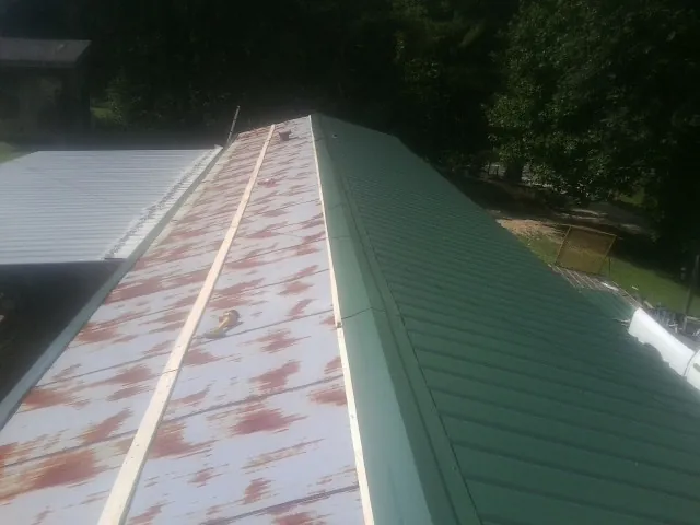 Old rusted panels beside newly installed green metal roofing — Wind Damage Roof Repair by Roofing Brothers in Cincinnatus