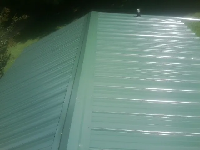New green metal panels meeting at the ridge of a roof — Flat Roof Repair work by our crew in Cincinnatus