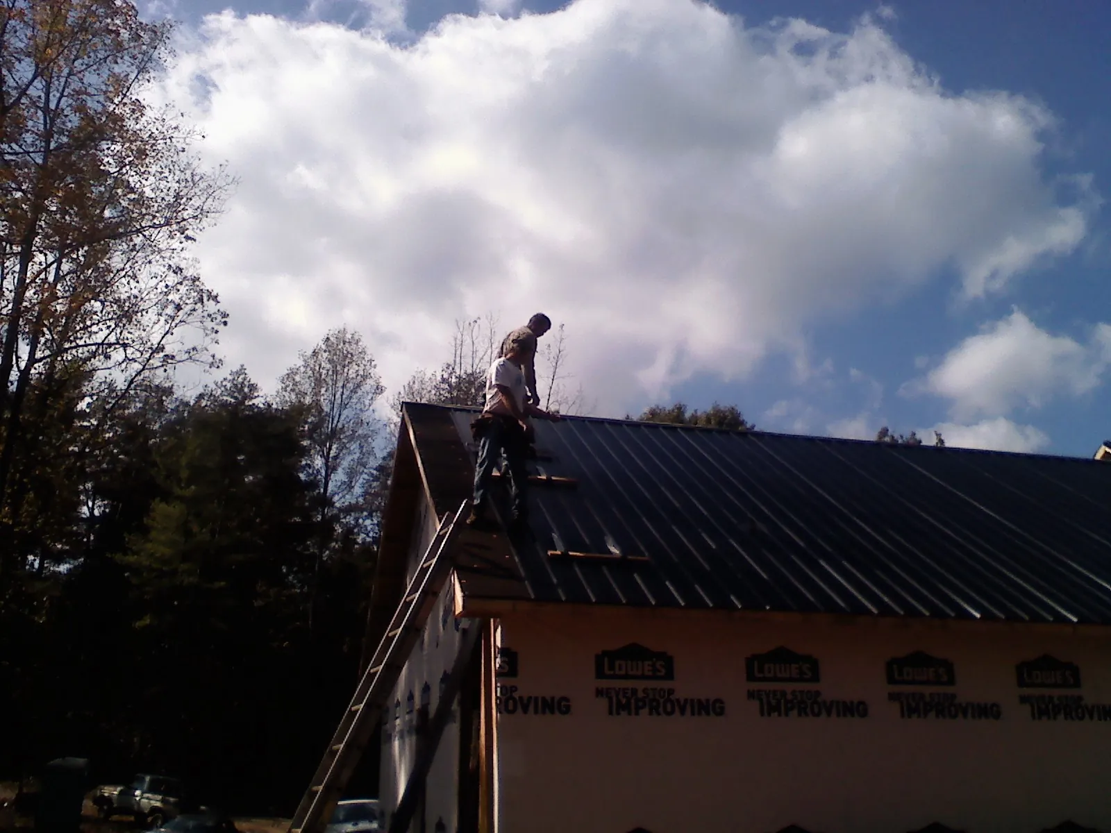 Roofer fastening dark metal panels high against a cloudy sky, from a Roof Inspection job in Cincinnatus