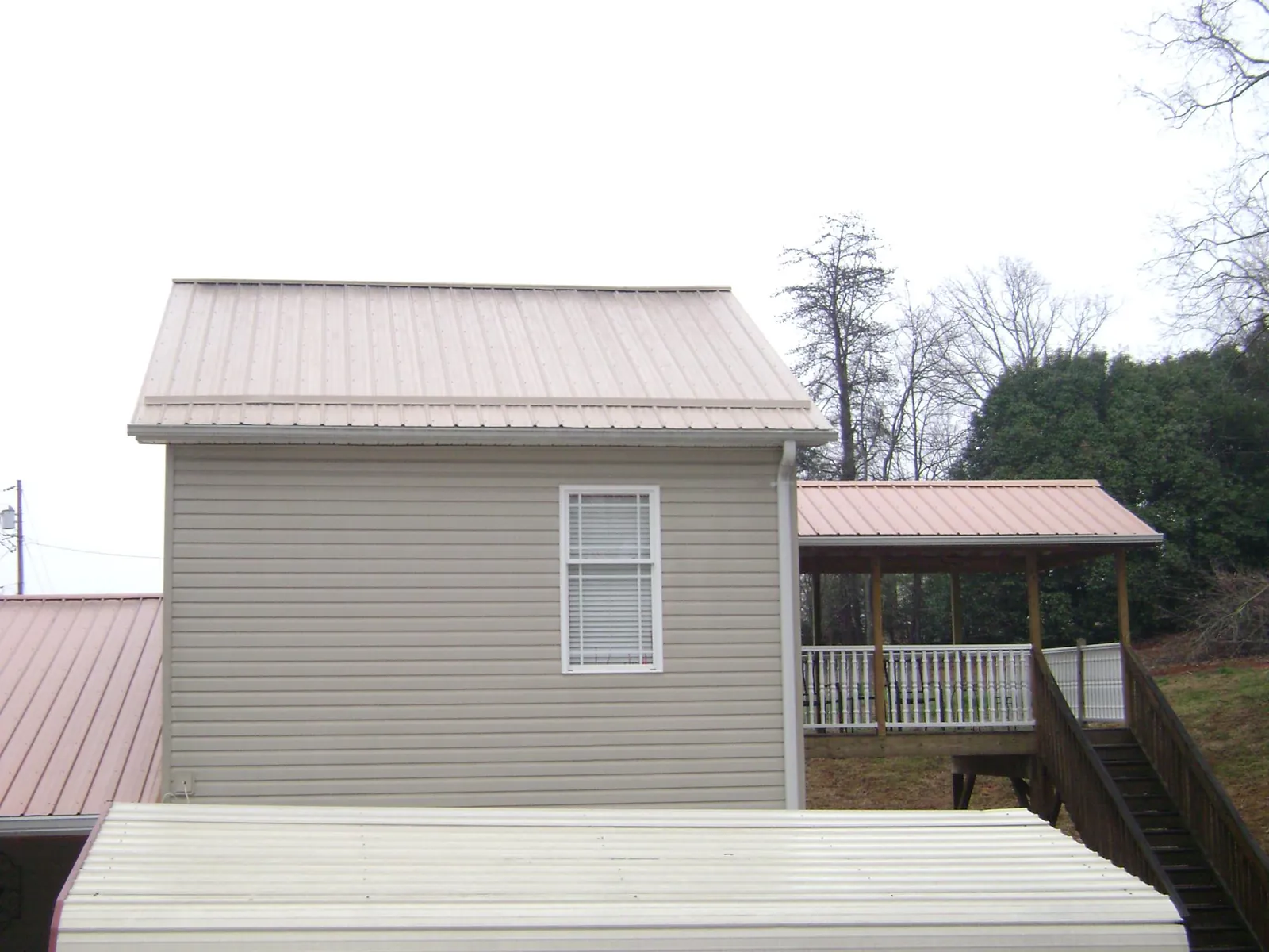 Tan metal roofs on a two story addition and attached porch, from a Roof Replacement job in Cincinnatus